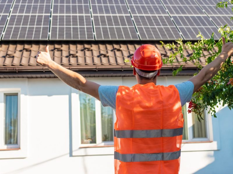Engineer Showing Thumbs Up at Solar Panels on House Roof.